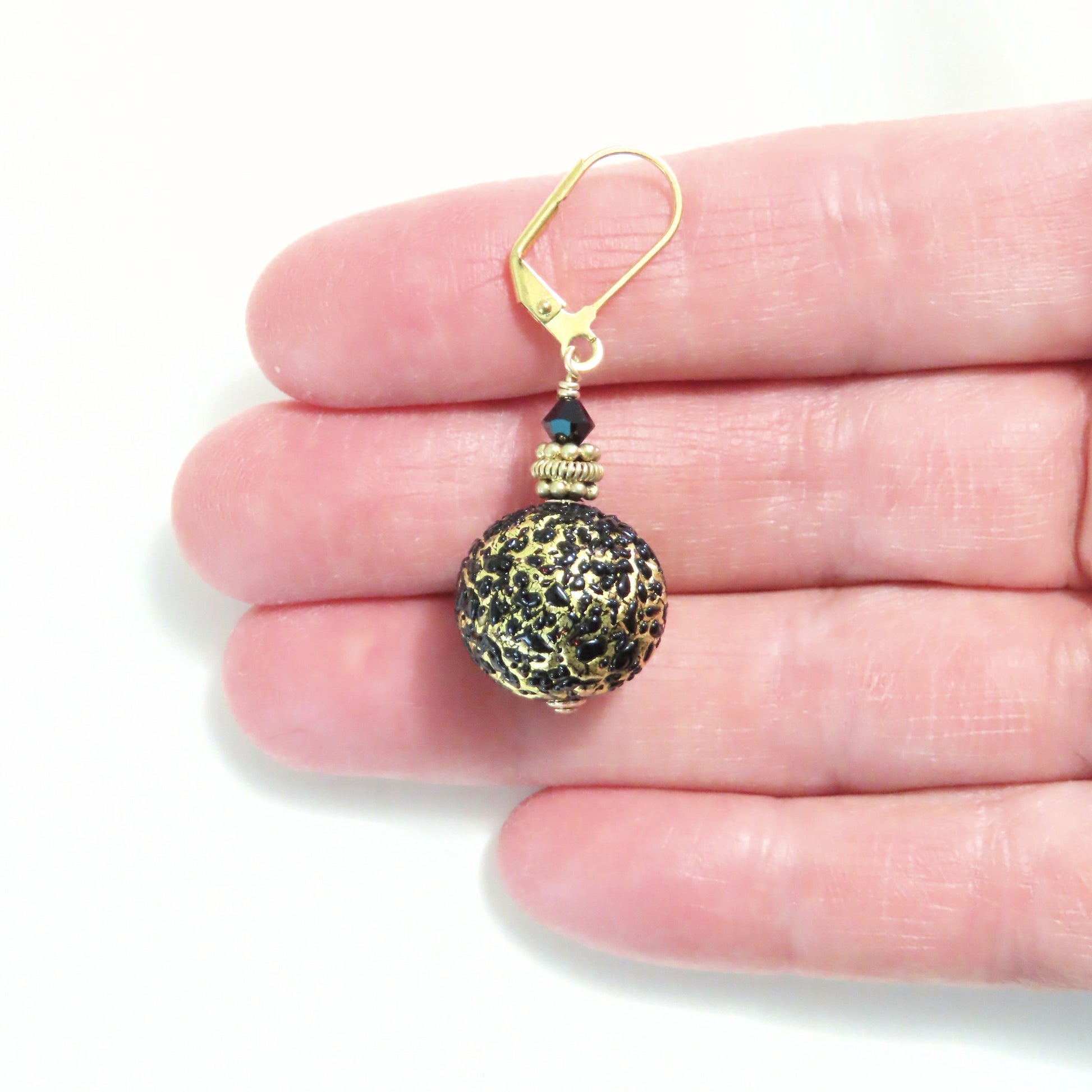 a hand holding a small gold and black bead charm